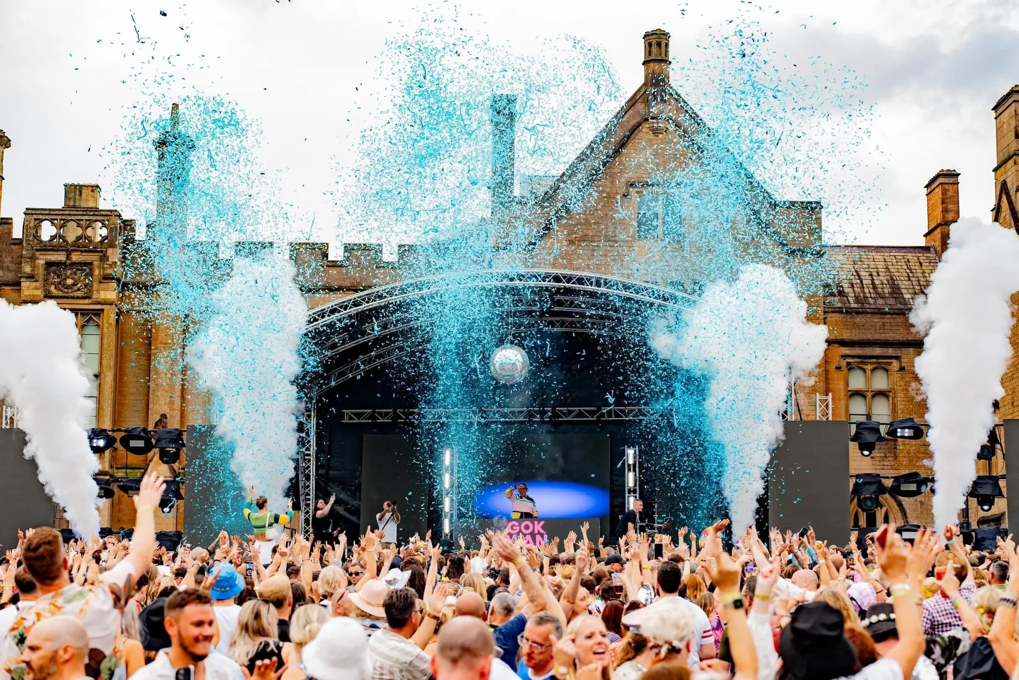 Festival crowd cheering as blue confetti and smoke cannons explode.