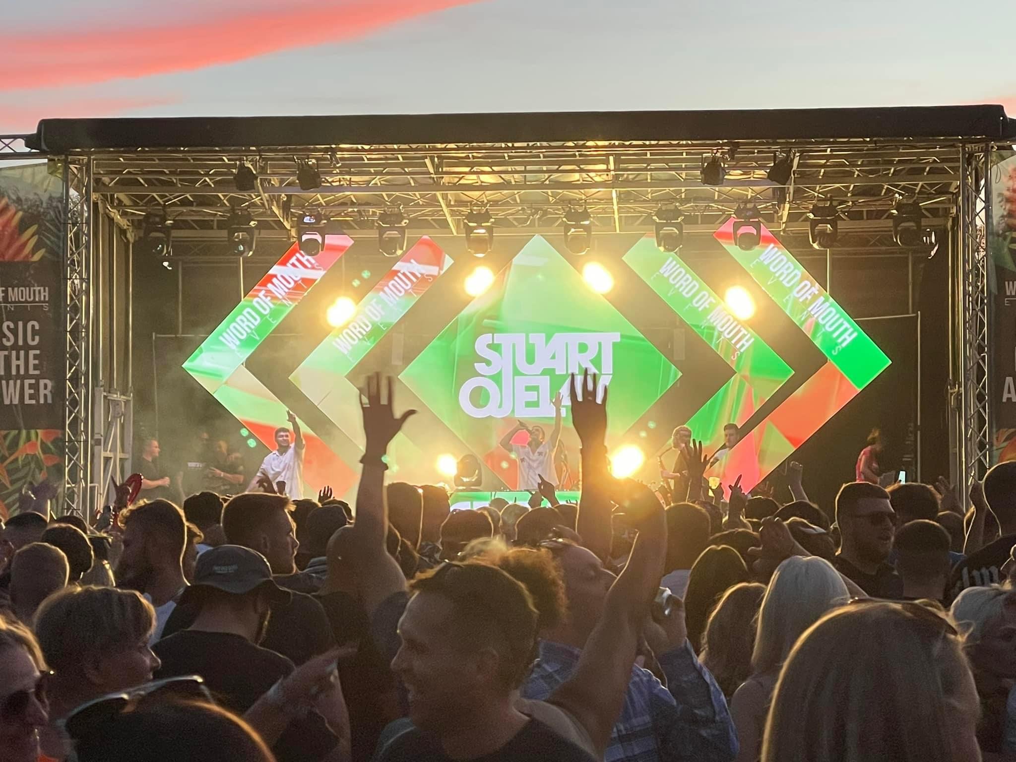Outdoor music festival stage with colorful LED screens and cheering crowd.